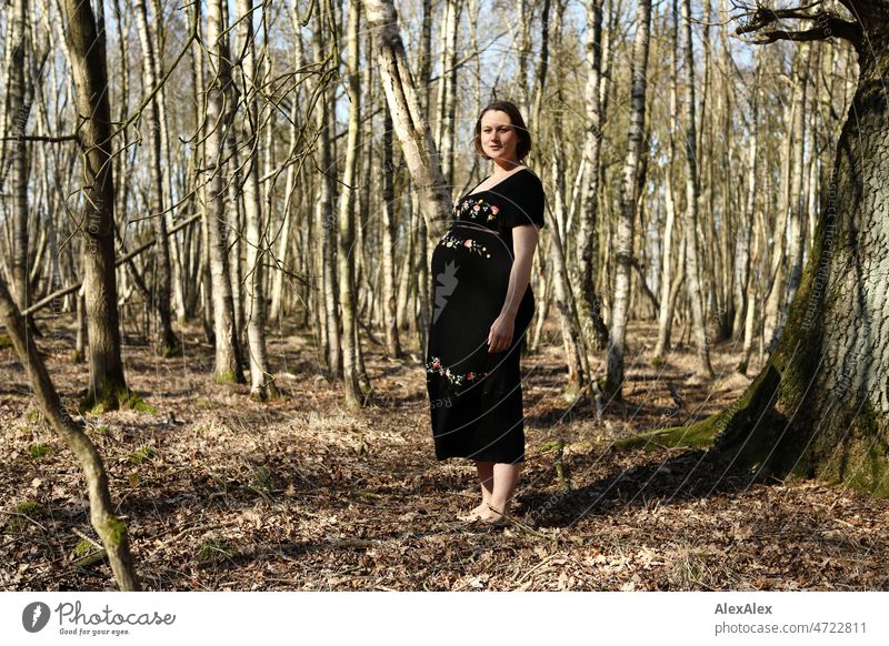 Junge, schwangere Frau steht in schwarzem Umstandskleid barfuß im Wald junge Frau schön Schönheit neues Leben Kleid Schwangerschaftsfoto Bauch Babybauch