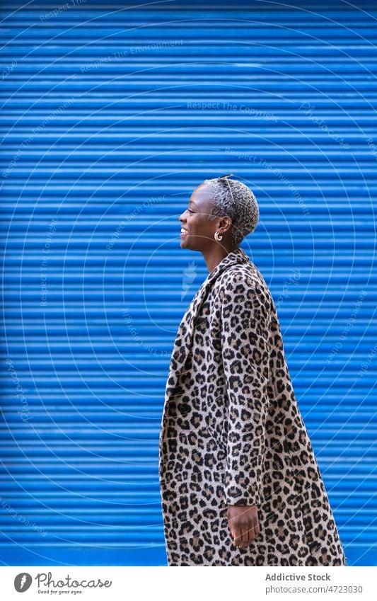 Positive schwarze Frau in der Nähe der blauen Wand Straße Stil Vorschein Outfit trendy Großstadt urban Kleidungsstück Lächeln Afroamerikaner froh Inhalt Glück