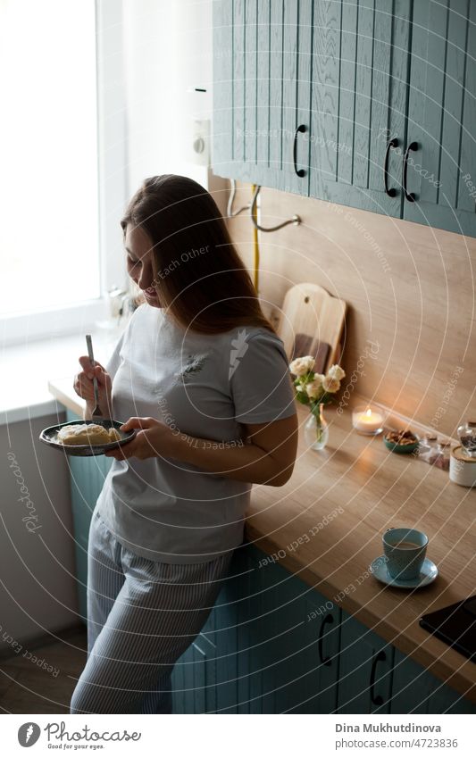 junge Millennial-Frau, die morgens in der Küche stehend ein Dessert isst und in den neuen Tag hineinlächelt Morgen gute Miene zum bösen Spiel offen