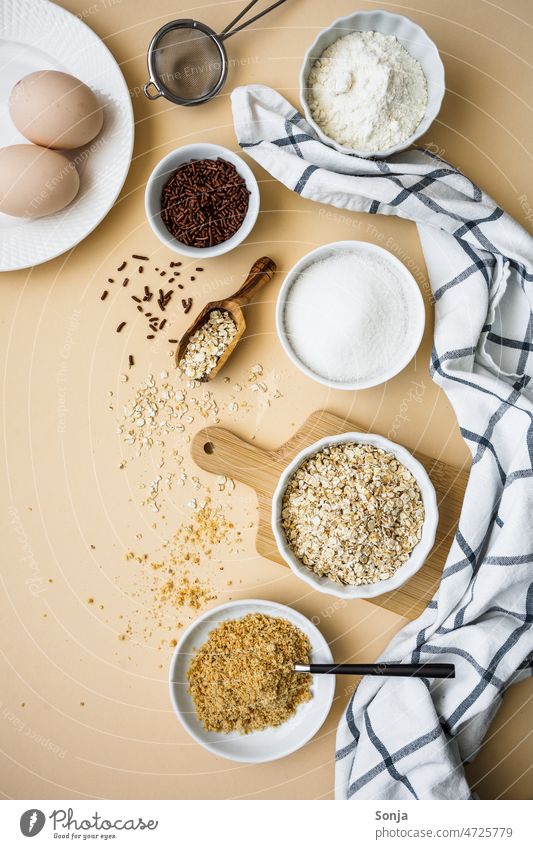 Backzutaten in weißen Schüsseln auf einem beigen Hintergrund. Draufsicht. Zutaten backen Kuchen Vorbereitung Mehl eier Zucker Haferflocken Frühstück roh