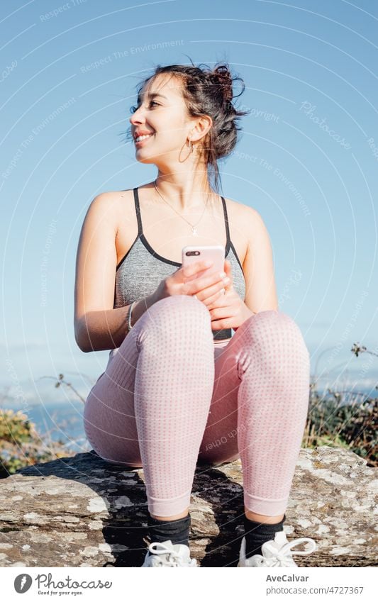 Junge Frau in Sportkleidung im Freien, die nach dem Training ihr Smartphone überprüft. Sorglos, positiv und Freiheit Konzept. Gesunder Lebensstil beim Sport im Freien. Super Lächeln mit zuversichtlicher Haltung