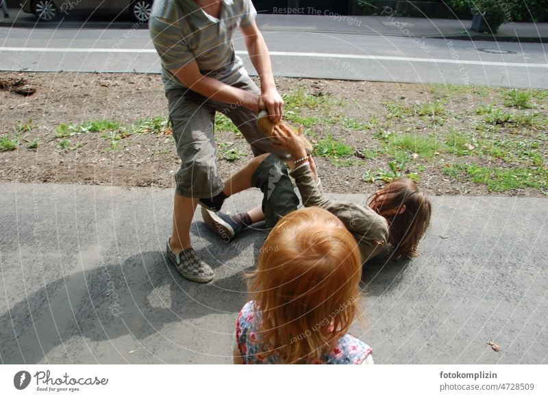 zwei Jungs raufen auf einem Bürgersteig und ein rothaariges Mädchen schaut zu kämpfen Kinder Jungen Kindheit Kinderspiel Soziales Leben Spielen Spaß spielerisch