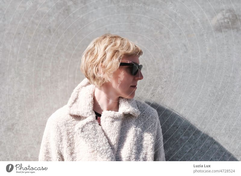 Eine blonde Frau mit Sonnenbrille genießt die Frühlingssonne modern Stil Dame Mode kuschelig Mantel attraktiv Lächeln elegant feminin Erwachsene kurzhaarig