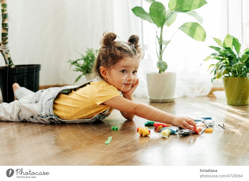 Ein reizendes kleines Mädchen modelliert aus farbiger Knete auf dem Boden. Hausunterricht, kreative Freizeitgestaltung mit Kindern Baby spielen heimwärts