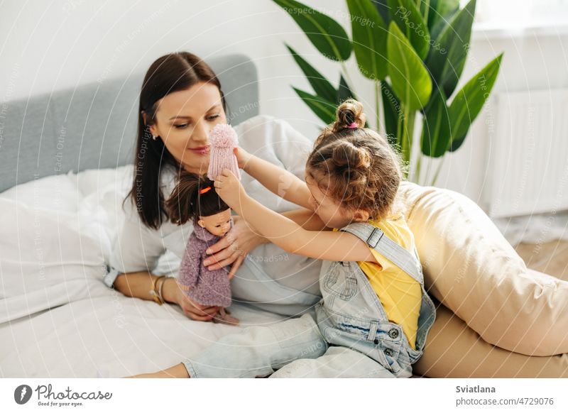 Mutter und kleine Tochter sitzen auf dem Bett und spielen mit Puppen. Mutterschaft, Fürsorge, gemeinsame Zeit Mama Tag hübsch Mädchen Porträt Familie Glück Kind