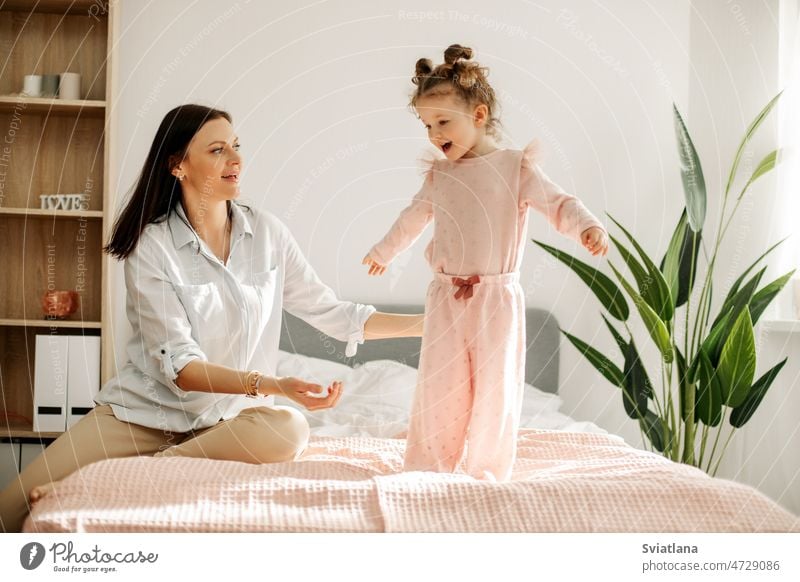 Eine junge Mutter spielt mit ihrem Baby im Schlafzimmer. Glückliche, liebevolle Familie. Mama Bett Spielen Spaß Mädchen Kind Porträt lustig Fröhlichkeit