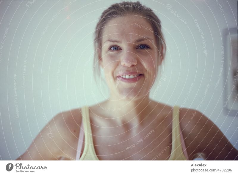 analoges Portrait einer jungen, großen, blonden Frau mit Grübchen, die in die Kamera lächelt schön schlank ästhetisch sportlich hochgewachsen fit natürlich