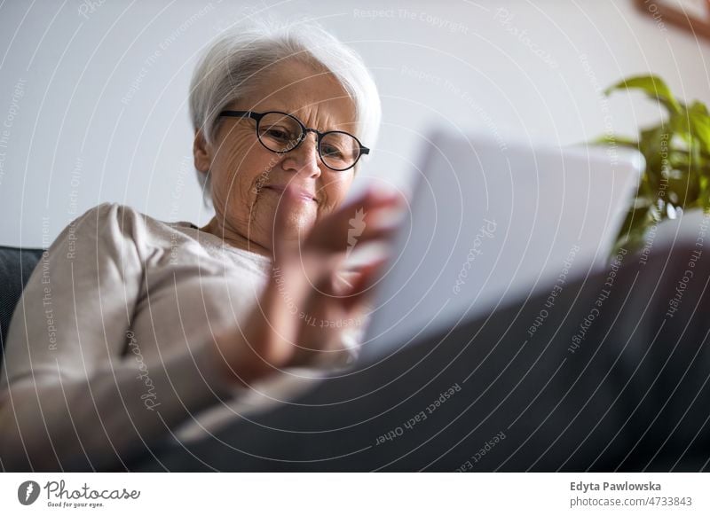 Ältere Frau benutzt ein digitales Tablet zu Hause Tablette digitales Tablett online Internet modern Technik & Technologie Mitteilung Anschluss Wohnzimmer Brille