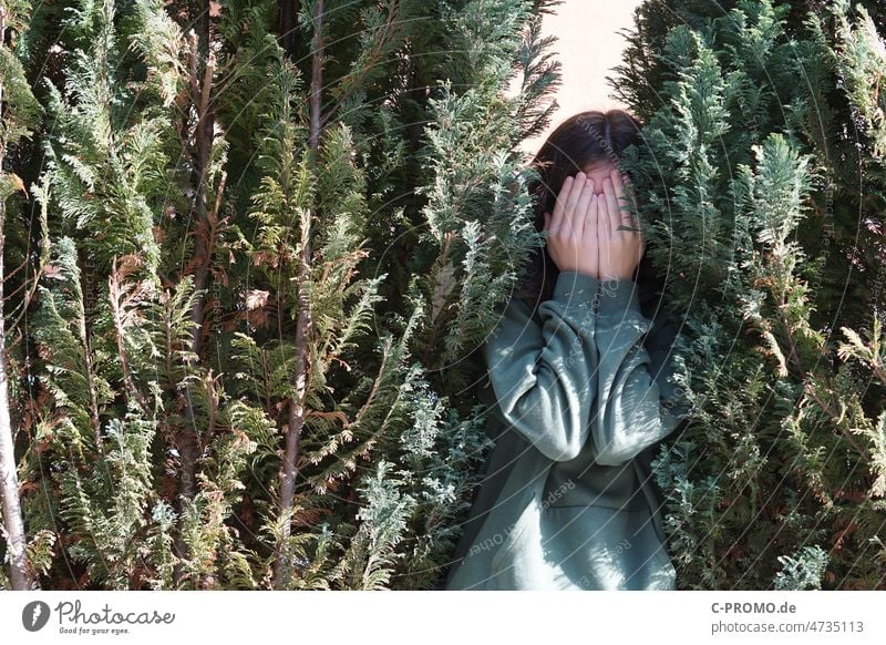 Teen versteckt sich zwischen Hecke unsichtbar Mädchen grün verstecken nicht sichtbar unangenehm hände vor dem gesicht peinlich Versteckspiel Hide and Seek