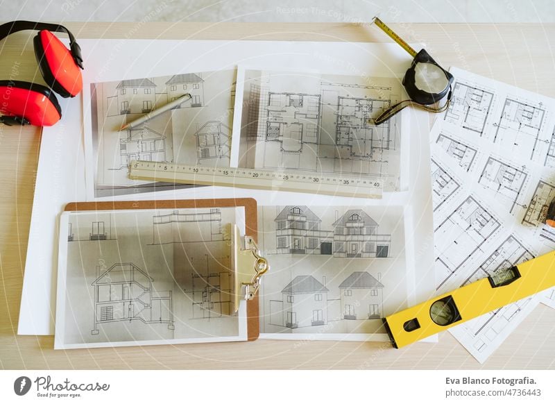 Draufsicht auf Baupläne, Ohrenschützer, Wasserwaage und Werkzeuge auf dem Arbeitsplatz eines Architekten auf der Baustelle Blaupausen heimwärts Niveau Meter