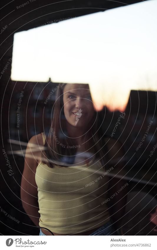 Portrait einer jungen, blonden Frau hinter einer Fensterscheibe, in der sich ein Haus und der Abendhimmel spiegeln lange Haare angenehm glücklich