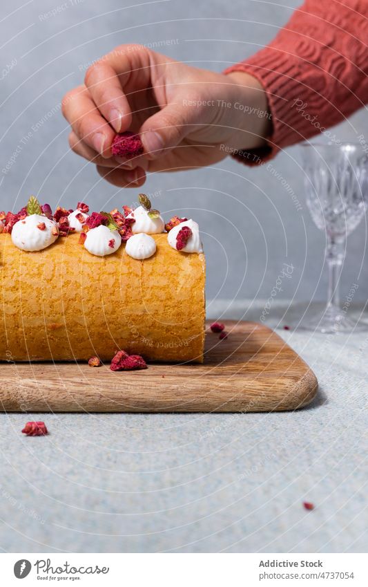 Frau, die getrocknete Himbeeren auf eine Rolle auf einem Holzbrett legt rollen Kuchen Dessert süß dienen Sahne selbstgemacht Rezept gebacken Beeren Zucker