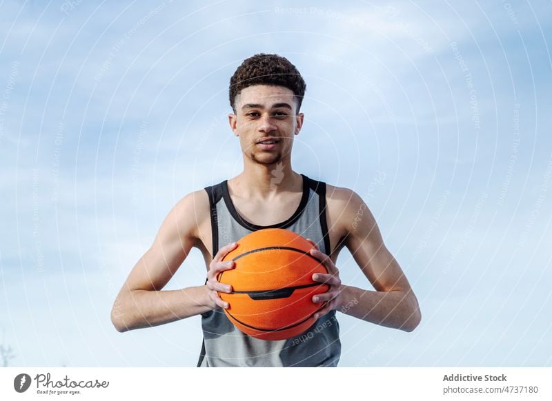 Hispanischer Mann mit Basketball schaut in die Kamera Sportler Ball spielen Training Spiel Gesunder Lebensstil Hobby Spieler Sportkleidung Straße Vorschein