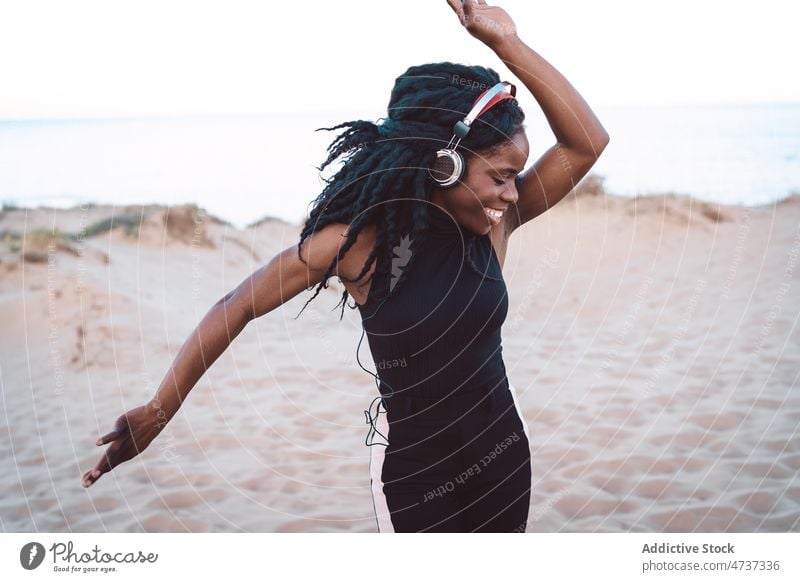 Unbekümmerte schwarze Frau hört am Strand Musik zuhören Tanzen Gesang Kopfhörer Sommer Meeresufer Spaß haben ethnisch Afroamerikaner sorgenfrei Freiheit