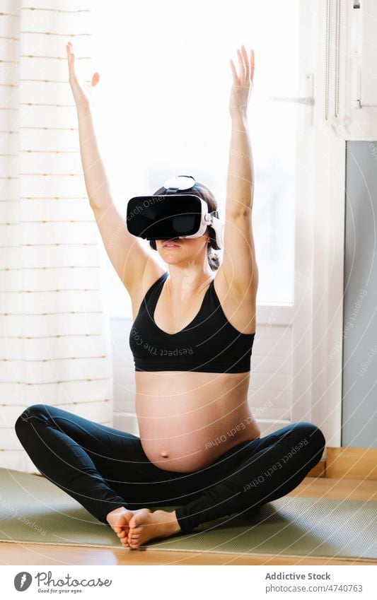 Lächelnde schwangere Frau meditiert mit VR-Brille zu Hause Yoga meditieren Cyberspace Virtuelle Realität Schwangerschaft heimwärts Schutzbrille Dehnung heiter