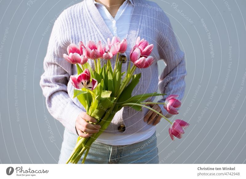 Teekesselchen | Strauß. Eine junge Frau mit Tulpen in der Hand steht vor einer hellen Wand Blumenstrauß Frühling Porträt posieren Licht und Schatten blühen