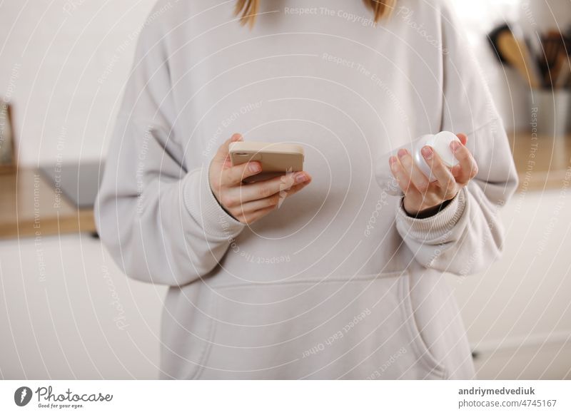 Frau, die Medizin nimmt. Junge Frau hält Flasche mit Pillen in der Hand und Lesen von medizinischen Anweisungen in das Handy. Kranke Frau Blick auf Medikamente Erklärung vor der Einnahme von verschreibungspflichtigen Medikamenten.