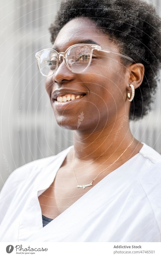 Zufriedene schwarze Frau mit Brille und Arbeitsuniform Straße Großstadt Vorschein Stil feminin urban Wand Uniform Afroamerikaner Sommer froh weiß genießen