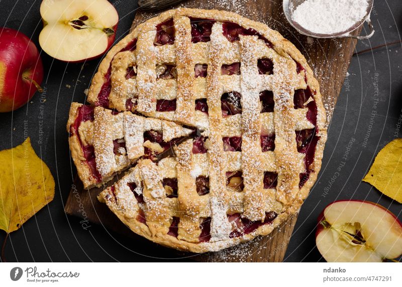 gebackener runder traditioneller Apfelkuchen auf braunem Holzbrett und frischen roten Äpfeln, Ansicht von oben Lebensmittel Frucht Pasteten Dessert