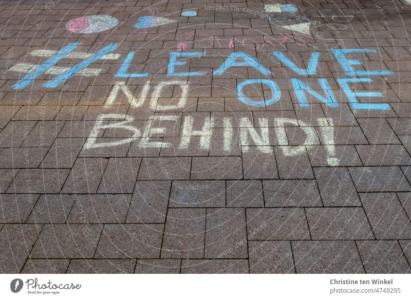 # LEAVE NO ONE BEHIND steht mit Strassenmalkreide in ukrainischen Farben auf einer gepflasterten Fläche Graffiti Pflastersteine Ukraine Solidarität Hoffnung