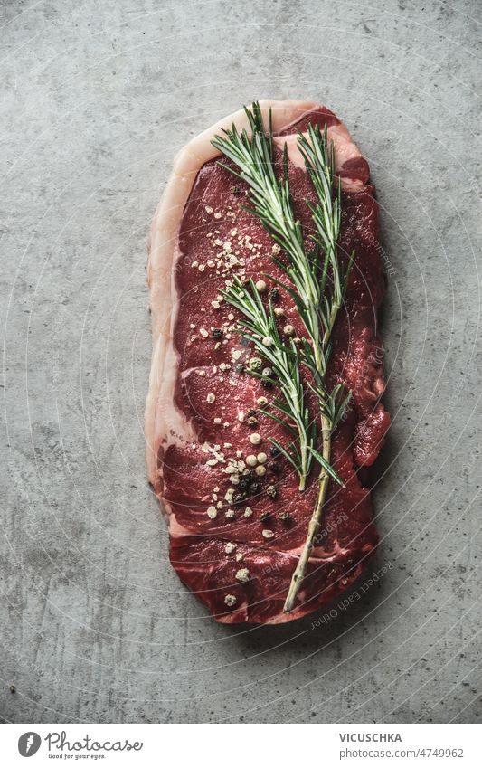 Rohes Rindersteak mit Pfeffer und Rosmarin auf grauem Hintergrund. roh Paprika Gewürz Fleisch geschmackvoll Zutaten Draufsicht angus Barbecue Rindfleisch