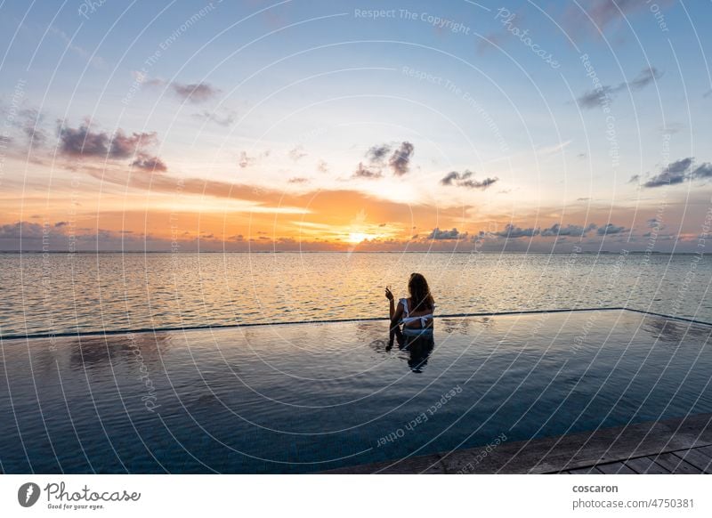 Attraktive Frau an einem Infinity-Pool in der Nähe des Ozeans mit einem Glas Champagner - Blick zurück allein Rücken schön Schönheit Cocktail genießend Abend