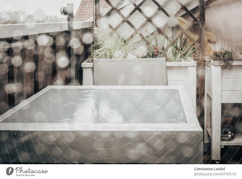 Balkontisch im Regen durch verregnete Scheibe gesehen. Wasser Wassertropfen nass feucht Regentropfen Fenster Fensterscheibe schlechtes Wetter Herbst kalt grau