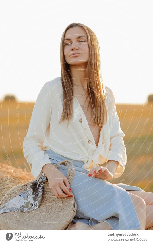 Schönes Porträt einer jungen Frau während des Sonnenuntergangs mit warmen gelben Sonnenstrahlen auf ihr Gesicht mit Strohballen auf dem Hintergrund ländlich