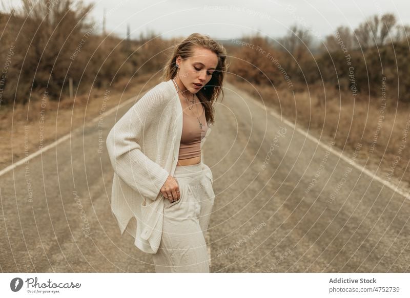 Stilvolle Frau auf der Straße stehend Landschaft Fahrbahn ländlich Vorschein feminin Autobahn Outfit attraktiv Windstille Porträt jung Asphalt Baum emotionslos