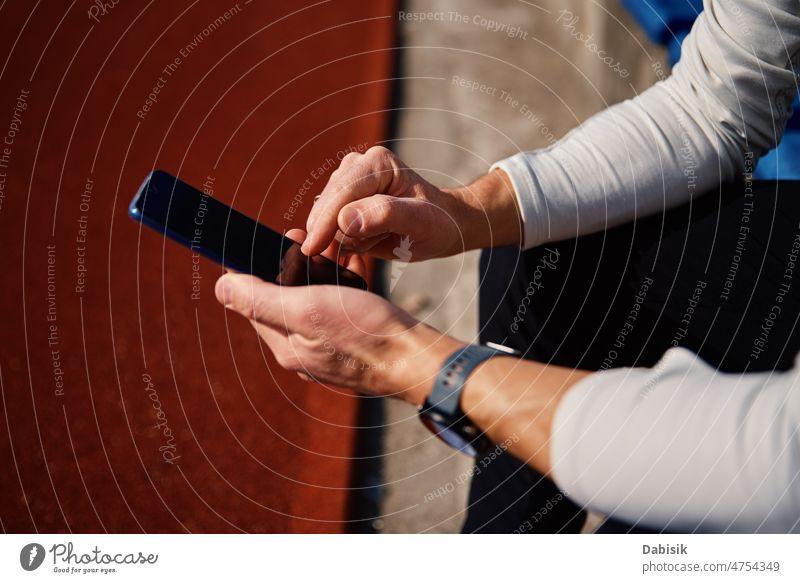 Mann in Sportkleidung ruht sich auf einem Stadionsitz aus und benutzt sein Smartphone aussruhen Fitness online Training im Freien Athlet Sportbekleidung