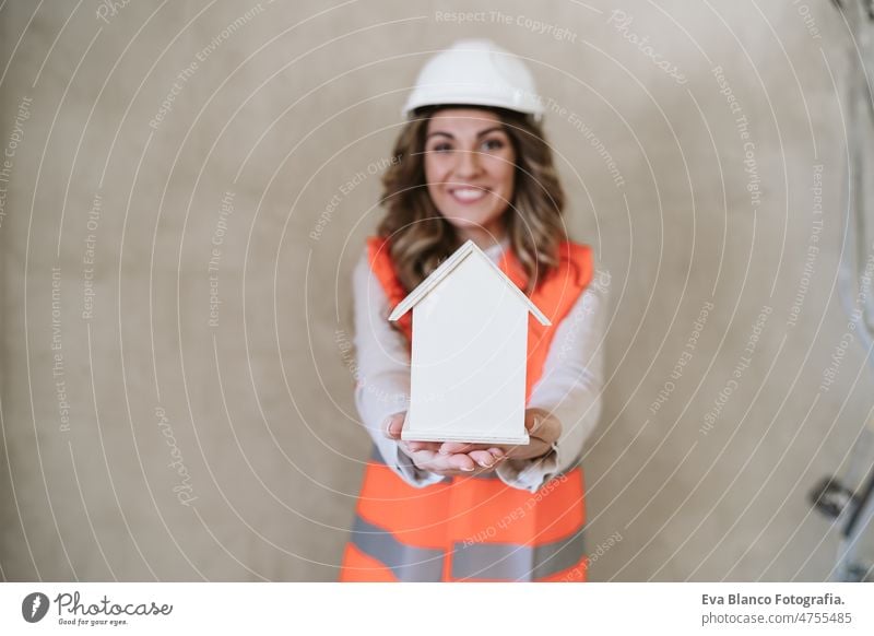 professionelle selbstbewusste Architektin auf der Baustelle mit Hausmodell. Hausrenovierung Frau Blaupausen Arbeitsbereich Schutzhelm Schutzmantel Handy