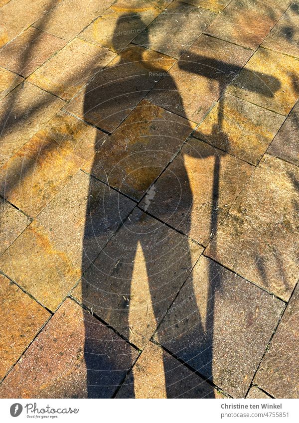 Pause machen beim Frühjahrsputz. Schattenmensch mit Besen in der Hand und nass glänzende Steinplatten auf einer Terrasse. Schattenfrau schattenmensch