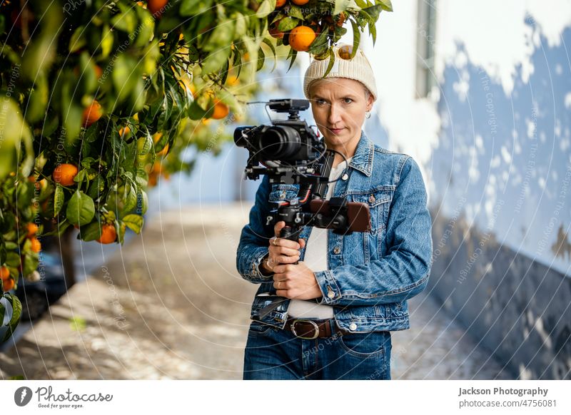 Kameramann mit Filmaufbau im Freien Filmemacher Video Betreiber Frau Gerät Mikrofon Fotokamera orange Orangenbaum Porträt Hipster Verschlussdeckel stabilisiert