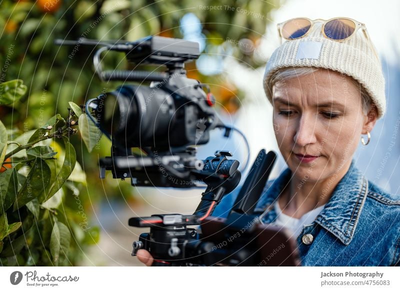 Kameramann mit Filmaufbau im Freien Filmemacher Video Betreiber Frau Gerät Mikrofon Fotokamera orange Orangenbaum Porträt Hipster Verschlussdeckel stabilisiert