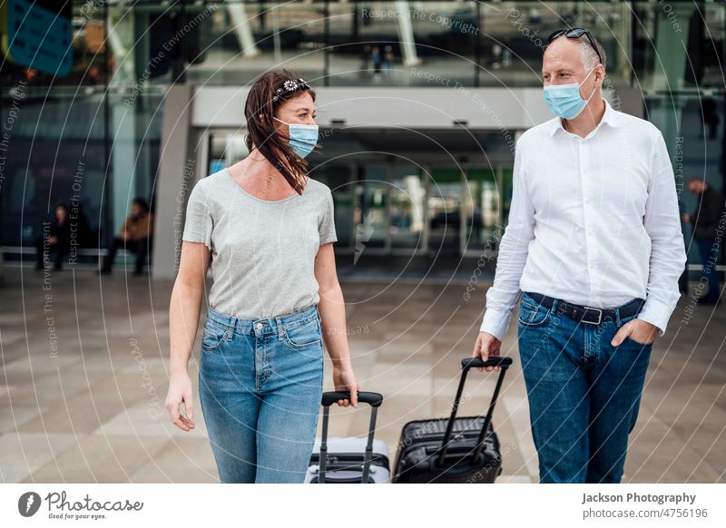 Reisende mit Schutzmasken unterhalten sich beim Verlassen des Flughafens mit ihrem Gepäck reisen Pandemie Mundschutz Frau Mann plaudernd Talkrunde reden Junge