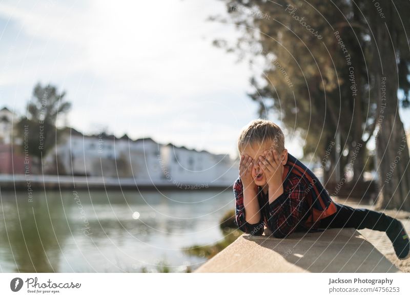 Niedlicher kleiner Junge, der in seiner Freizeit am Fluss Gesichter macht Kind Natur lustig Gesichter machen spielen Textfreiraum Kindheit sich[Akk] entspannen