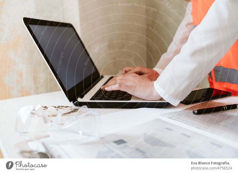 unerkennbare Architektin auf einer Baustelle, die mit Blaupausen und Laptop arbeitet unkenntlich Handy Frau Arbeitsbereich Schutzhelm Schutzmantel Grundbesitz