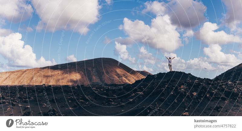 Frau hebt die Hände in den Himmel und genießt die atemberaubende Aussicht auf die Vulkanlandschaft im Timanfaya-Nationalpark auf Lanzarote, Spanien. Freiheit und Reise Abenteuer Konzept.