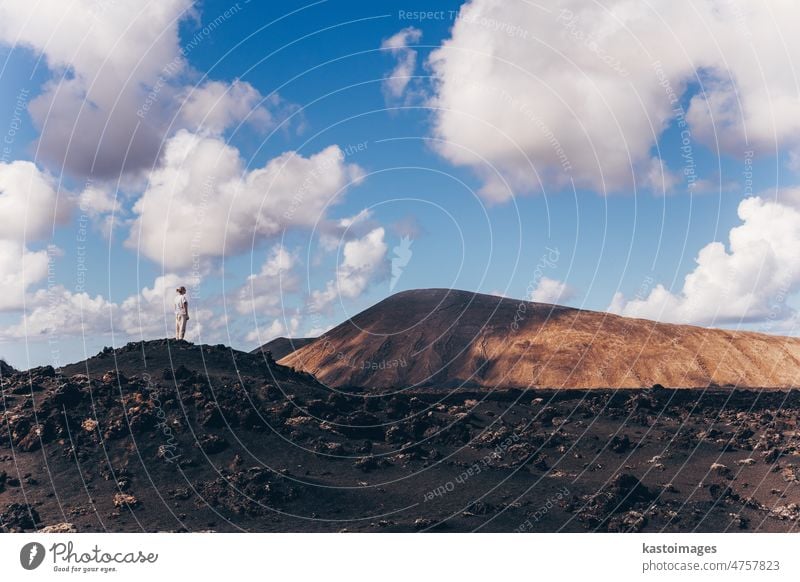 Frau hebt die Hände in den Himmel und genießt die atemberaubende Aussicht auf die Vulkanlandschaft im Timanfaya-Nationalpark auf Lanzarote, Spanien. Freiheit und Reise Abenteuer Konzept.