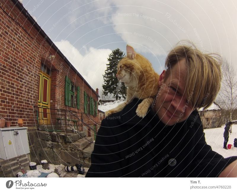 ein Mann mit einem Roten Kater auf der Schulter im Winter Bauernhof roter Kater Katze Polen Gutshof Schnee kalt Haustier Tier Fell Hauskatze Tierporträt