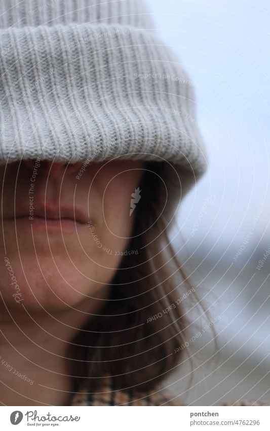 Eine schlecht gelaunte frau versteckt sich unter ihrer Mütze. Winterdepression, winterblues Frau mütze winterdepression symbolbild Einsamkeit traurig