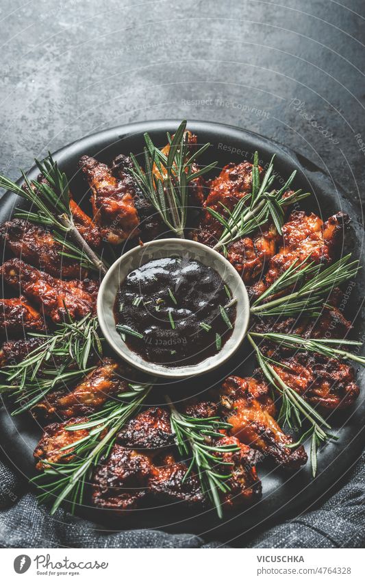 Hausgemachte gegrillte Hähnchenflügel mit BBQ-Sauce und Rosmarin selbstgemacht dunkel Beton Küche Tisch lecker Lebensmittel Grillrost mariniert Hühnerfleisch