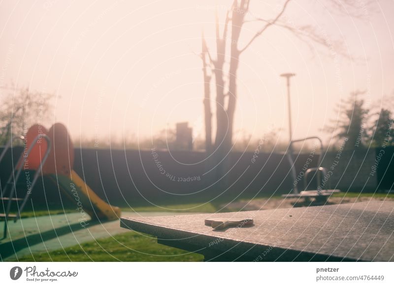 Ein Tischtennisschläger liegt auf einer Tischtennisplatte, im Hintergrund ist ein Spielplatz zu sehen. Spielen Kinder Freizeit & Hobby Sport Freude Rutsche