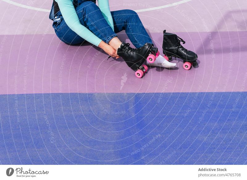 Anonyme Frau beim Anziehen von Rollschuhen auf einem Sportplatz Rollerskate Vierfachrolle Schlittschuh sportlich üben Hobby Lifestyle aktiv Sportpark Training