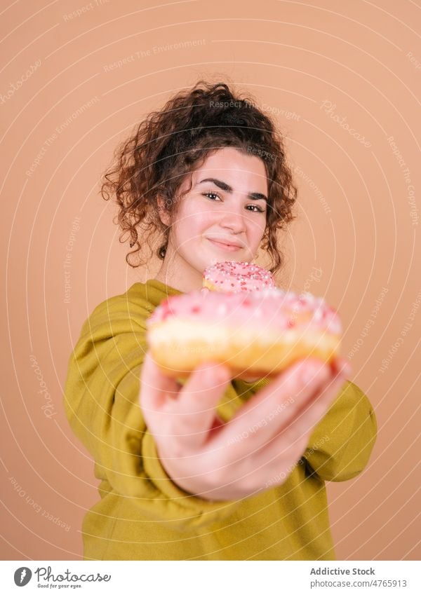 Glückliche Frau, die süße Donuts isst und in die Kamera schaut essen geben Dessert genießen Geschmack teilen lecker Zuckerguß Leckerbissen hungrig zuckerhaltig