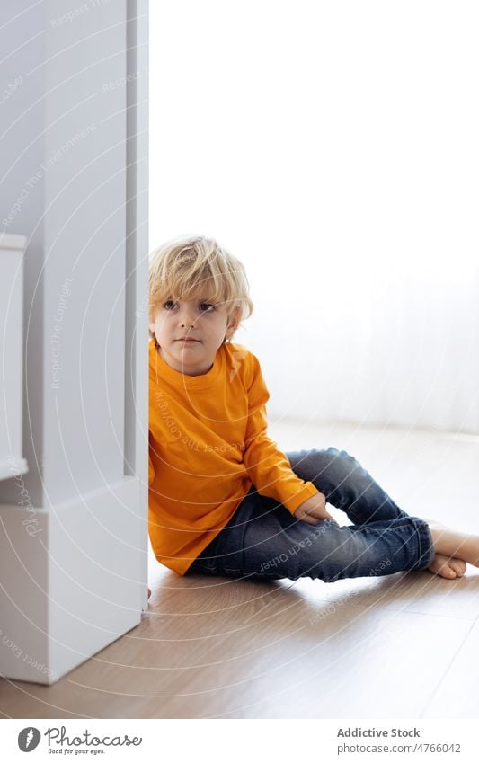 Niedlicher kleiner Junge sitzt auf Parkett in der Nähe der Wand Kind Kindheit neugierig Interesse heimwärts Appartement Raum niedlich erkunden Beine gekreuzt