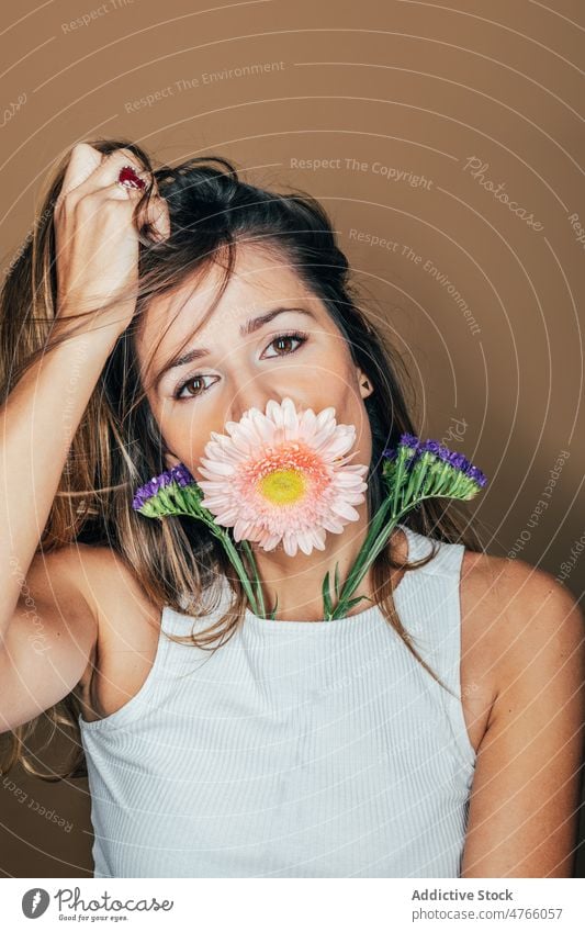 Frau mit Gerbera-Blüte im Mund im Atelier Blume Porträt Blütezeit sanft frisch feminin Model Angebot Vorschein charmant lange Haare Studioaufnahme Stil