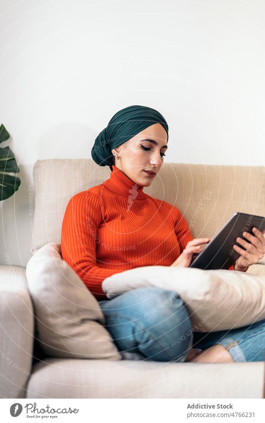 Muslimische Frau mit Tablet auf der Couch Porträt Tablette benutzend Sofa heimwärts Wohnzimmer soziale Netzwerke ruhen Wochenende online muslimisch ethnisch