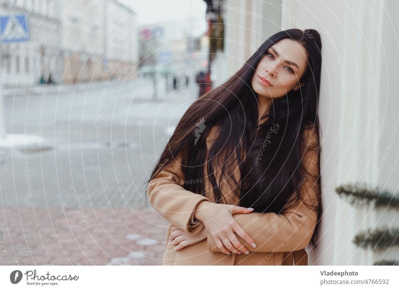 Junge brünette Frau in beigem Wintermantel steht allein auf der Straße Mode Mantel Kleidung Aussehen elegant Großstadt lang Behaarung jung Wand schön Lifestyle