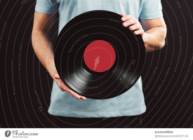 Mann mit Schallplatte. Vintage-Musik-Stil. Mann in blauem T-Shirt hält schwarze analoge Schallplatte auf schwarzem Hintergrund. Retro-Musik Aufzeichnen Vinyl